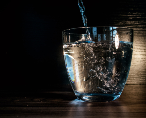 Water streams into a mostly full short glass, dramatically lit against a dark wood background