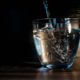 Water streams into a mostly full short glass, dramatically lit against a dark wood background